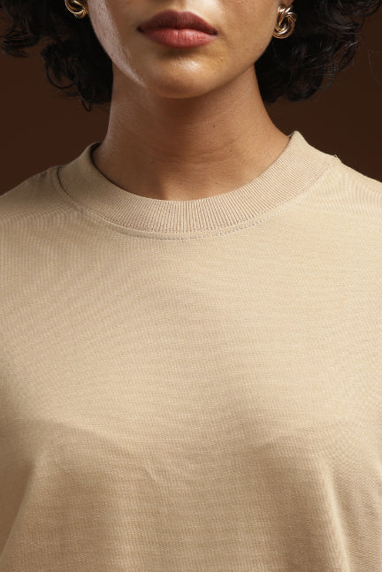ADEL & VIDA beige oversized t-shirt with a ribbed crew neckline worn by a model with gold hoop earrings.