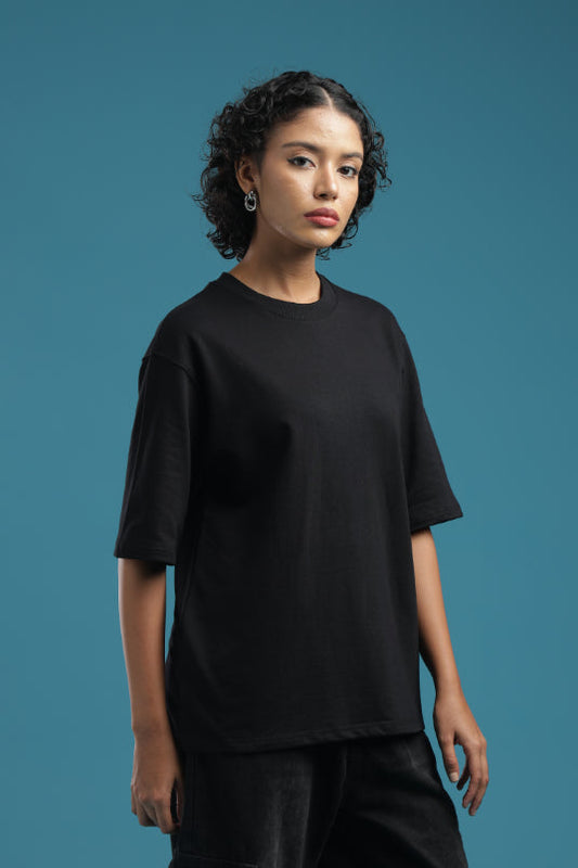 Model wearing an ADEL & VIDA black oversized t-shirt with a soft, breathable fabric against a blue background.