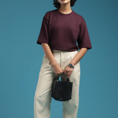 ADEL & VIDA burgundy oversized t-shirt worn by a model with beige trousers and glasses against a blue background.