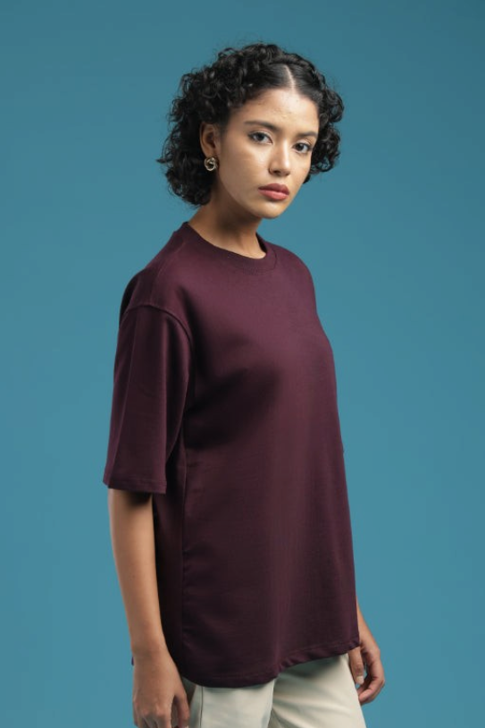 Model wearing an ADEL & VIDA burgundy oversized t-shirt with a soft, minimal design against a blue background.