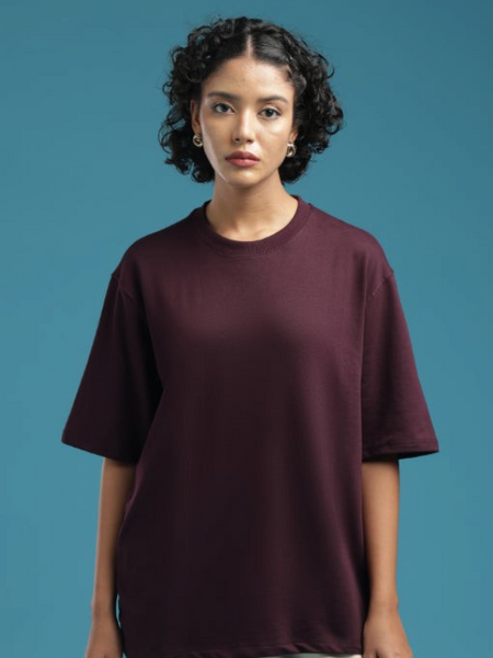 Model wearing an ADEL & VIDA burgundy oversized t-shirt with a soft, minimal design against a blue background.