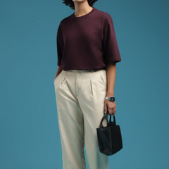 ADEL & VIDA model wearing an oversized burgundy t-shirt with cream trousers and glasses against a blue background