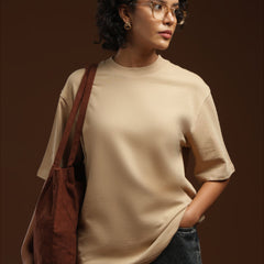 ADEL & VIDA model wearing an oversized beige t-shirt with a brown corduroy tote bag against a dark brown background