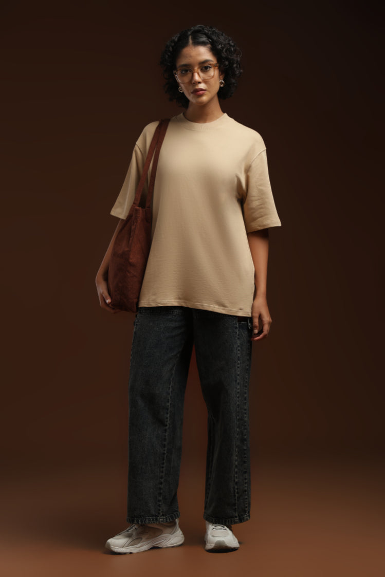 ADEL & VIDA oversized beige t-shirt worn by a woman with dark curly hair, paired with dark jeans and a brown tote.