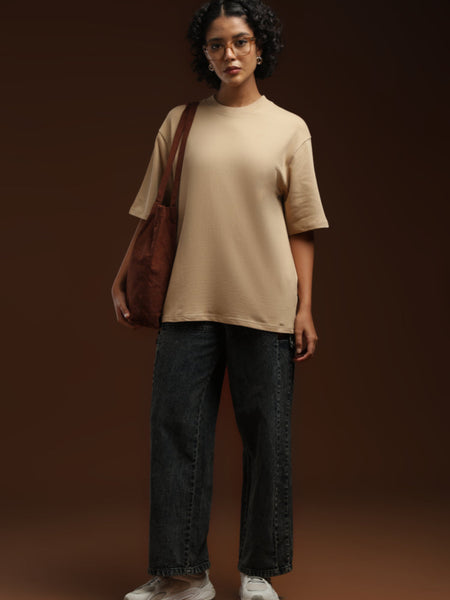 ADEL & VIDA oversized beige t-shirt worn by a woman with dark curly hair, paired with dark jeans and a brown tote.